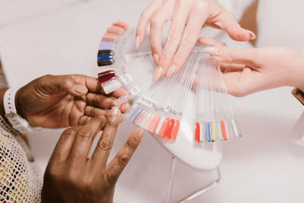 Hands holding acrylic nail samples of various colors