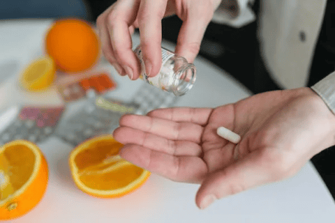 Person with vitamin in palm and oranges on table - alopecia caused by vitamin deficiency