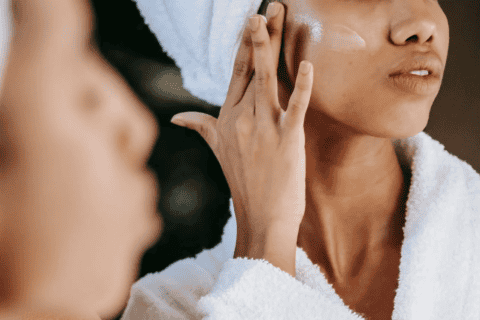Individual in white towel applying lotion to upper cheek
