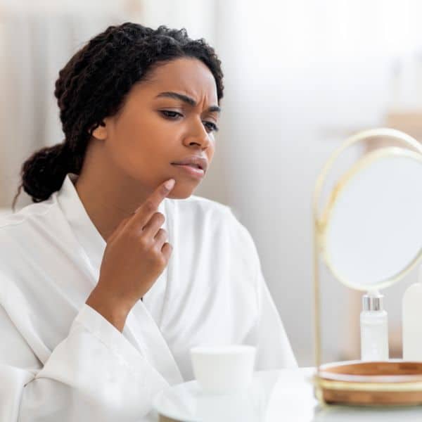 Black woman looking on mirror showing frustrations on skin