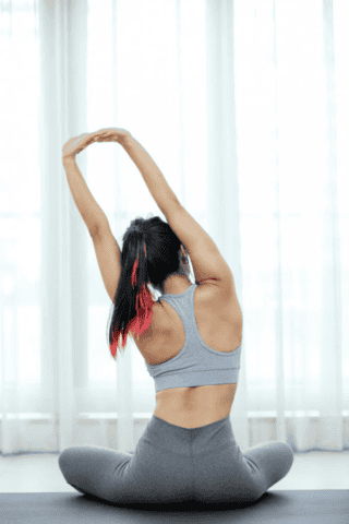 Back view of individual with ponytail stretching arms in sitting position