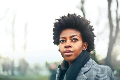 A woman wearing a coat and scarf walks outside.